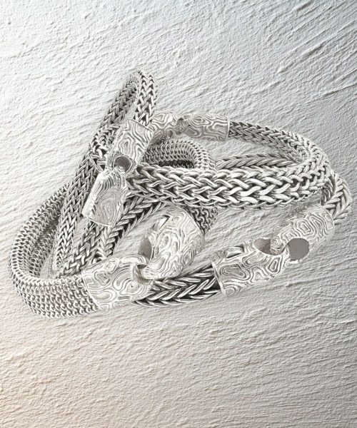 Handcrafted men’s silver chain bracelets arranged on textured mineral plaster background.