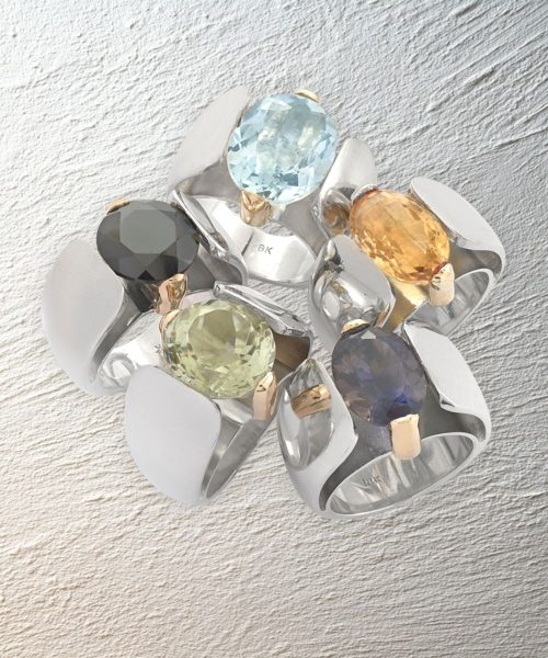 Cluster of women’s gemstone rings in silver with mixed colored stones on textured plaster background.