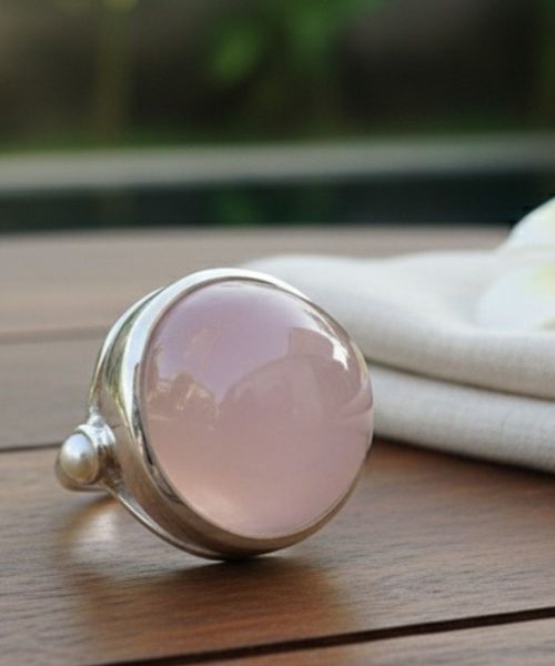 Rose quartz cabochon silver ring resting on wooden surface